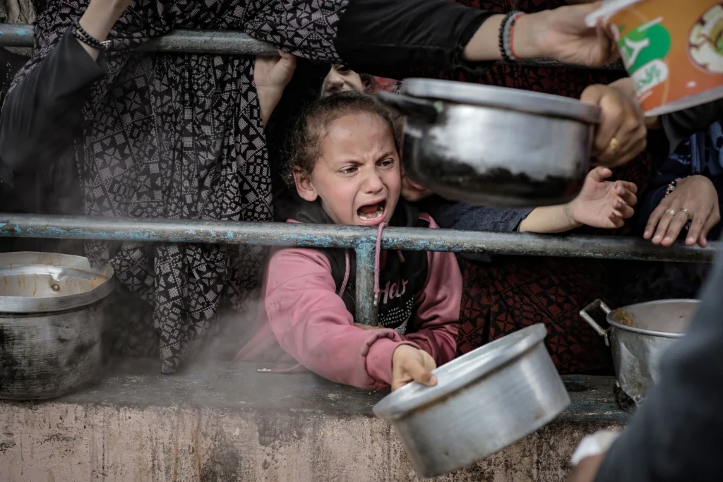 Palestinian children in Rafah wait in line on Feb. 10 among the rubble of destroyed buildings to receive food prepared for Palestinian families displaced to southern Gaza due to Israeli attacks.