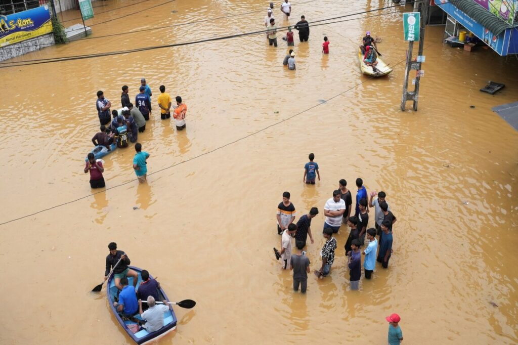 people use boats to move on a flooded street as others stand around, following heavy rainfall in malwana